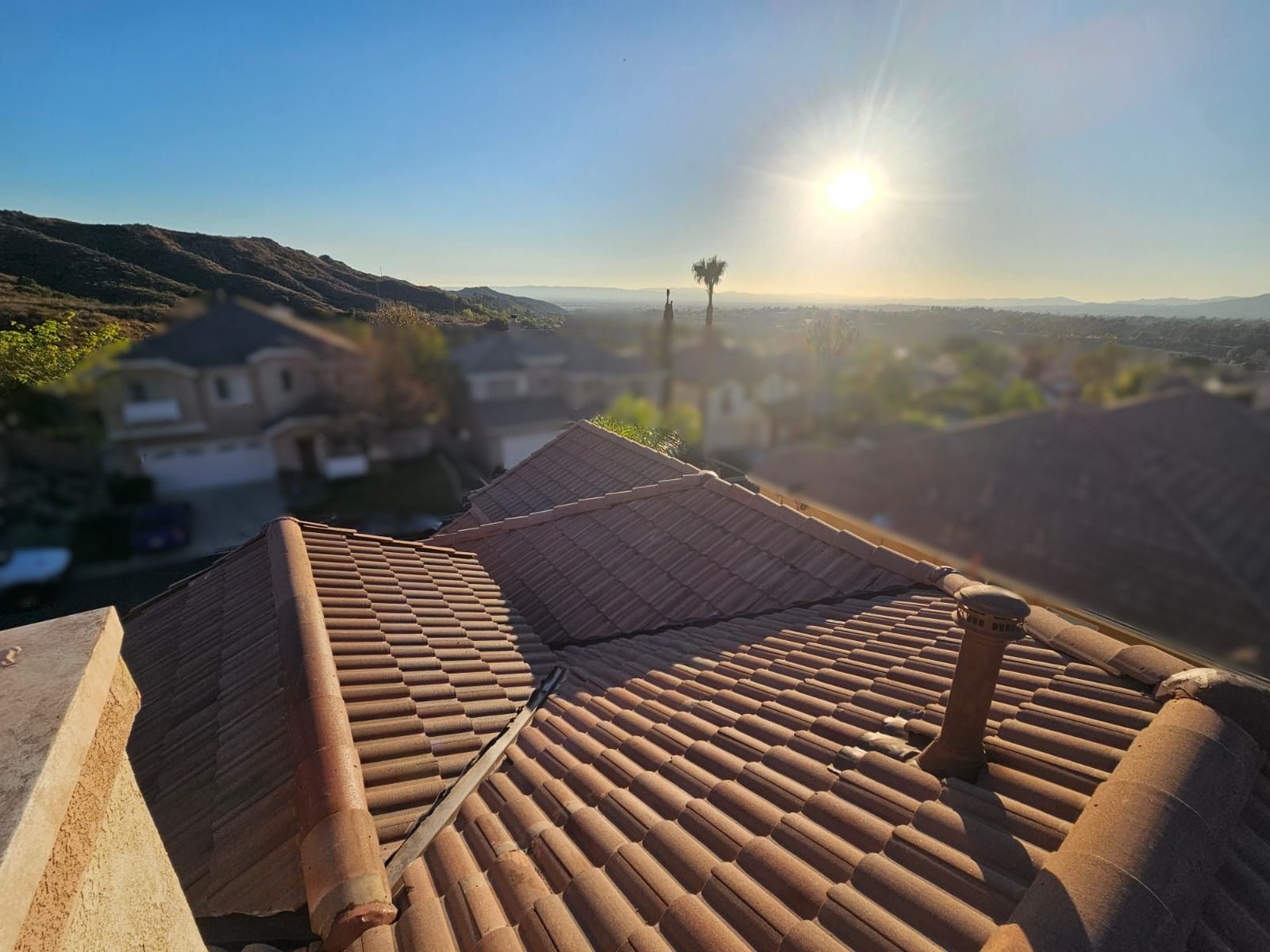 Tile roof with sun shining over suburban homes and hills.