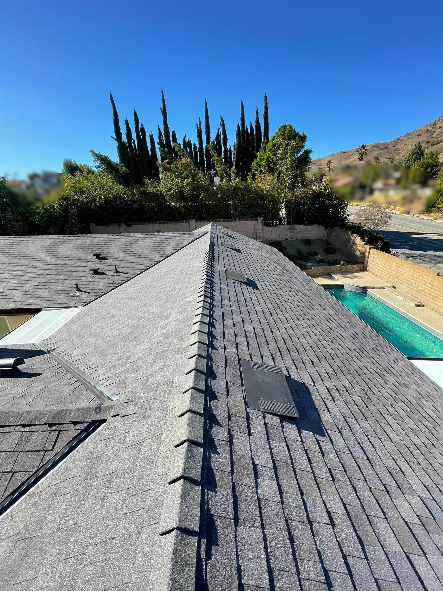Gray shingled roof, pool in background, trees and a blue sky.