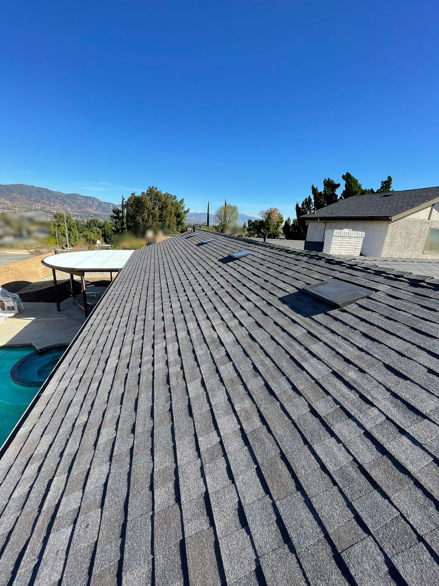 Gray shingle roof with a pool and mountains in the background under a clear blue sky.