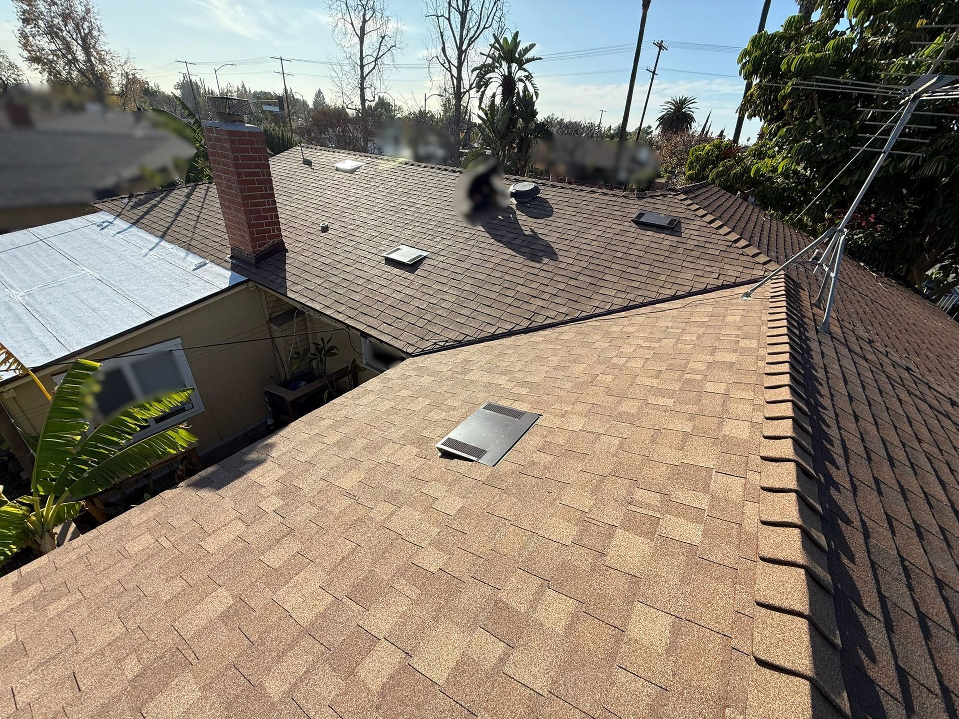 Overhead view of a brown shingle roof on a house with a chimney and vents, under a bright sky.