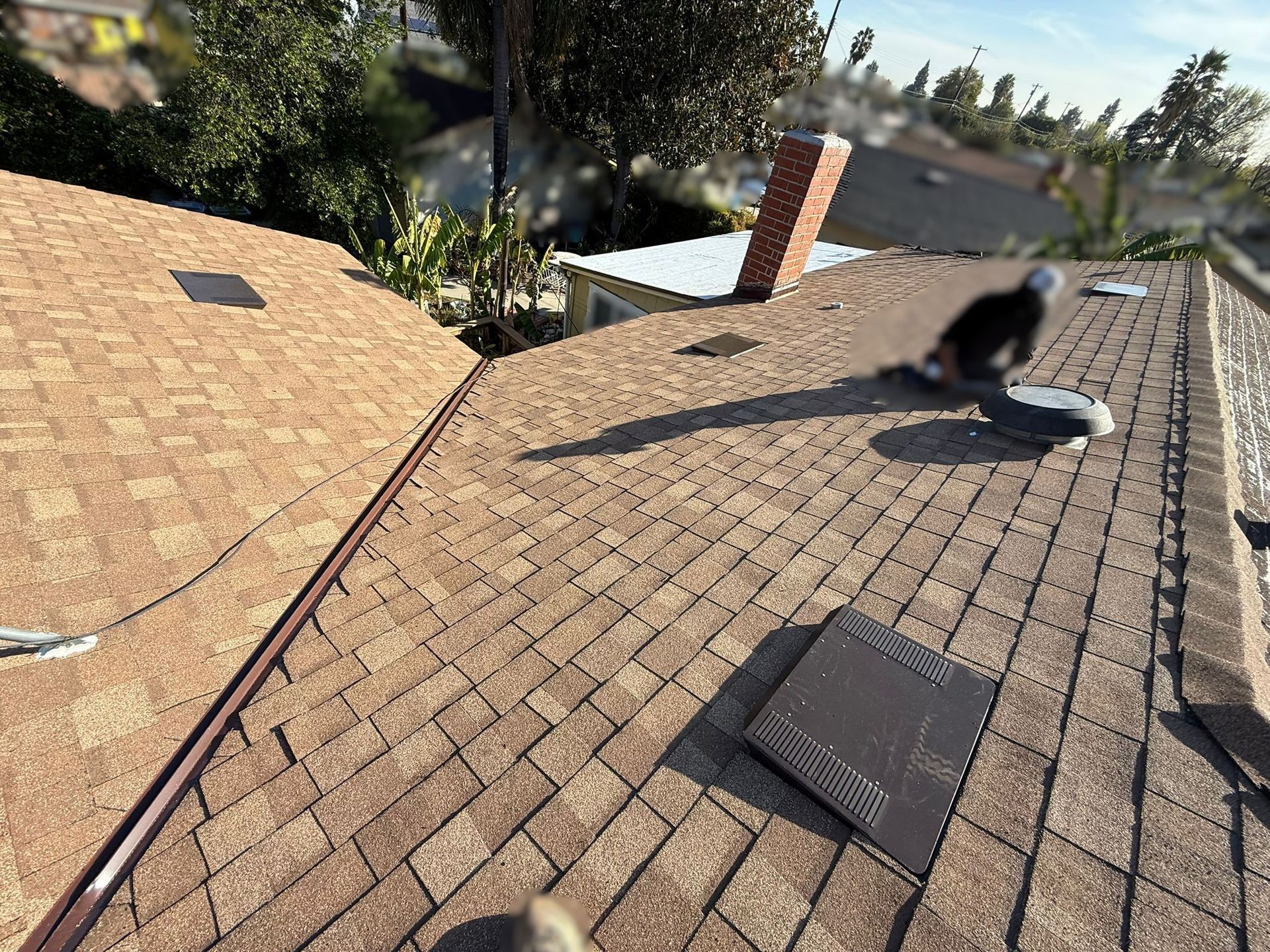 Person on a roof with brown shingles, a brick chimney, and blue sky.