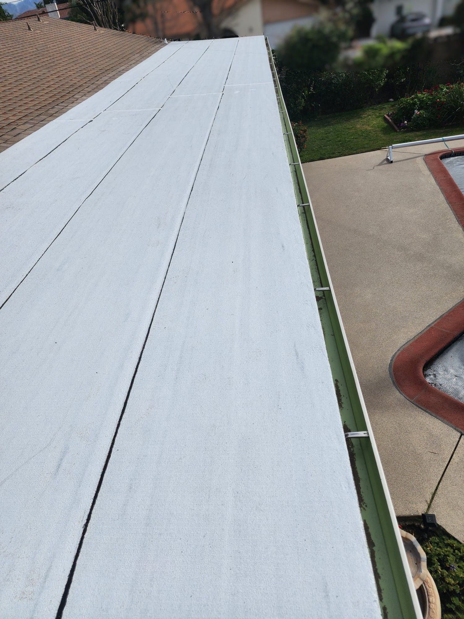 White flat roof with black lines and a green gutter, next to a patio.