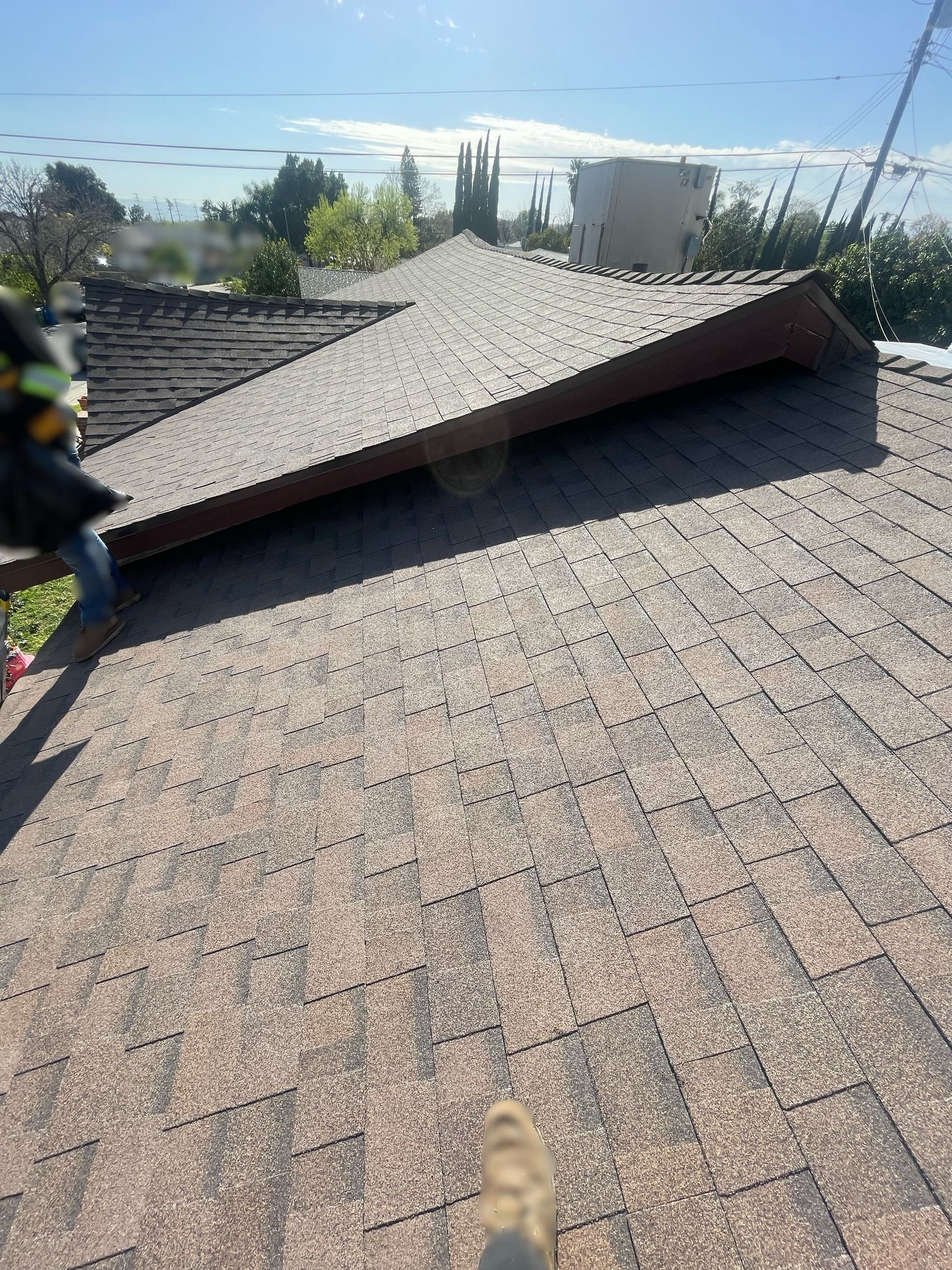 View of a brown shingle roof with a small dormer, person working, bright sunlight.