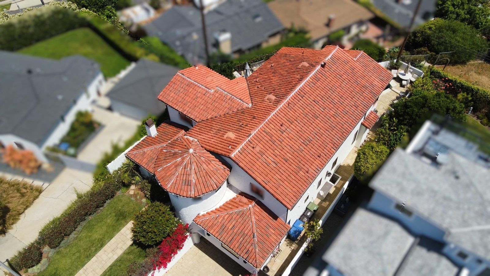 Aerial view of a white house with a red-tiled roof, surrounded by greenery and other houses.
