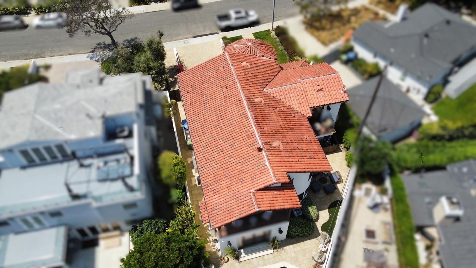 Aerial view of a house with a red tile roof, surrounded by trees and other houses on a sunny day.