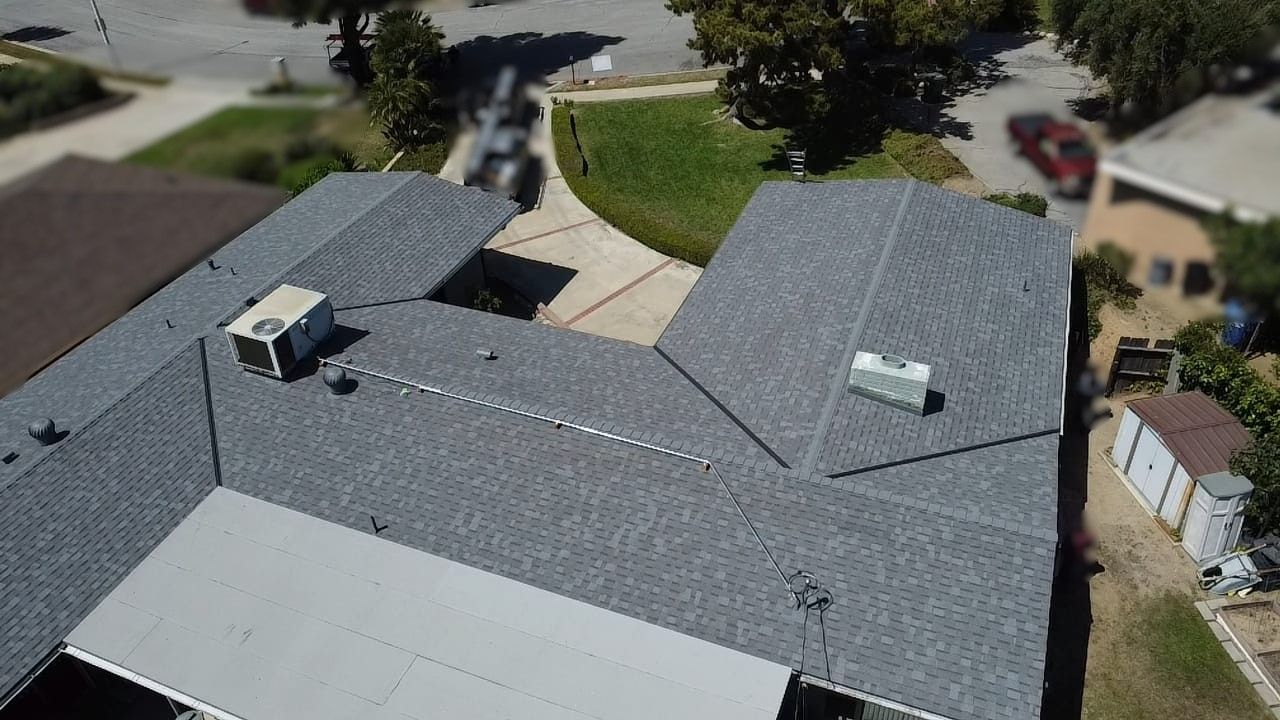 Aerial view of a gray-shingled house with a driveway, surrounded by grass and trees.