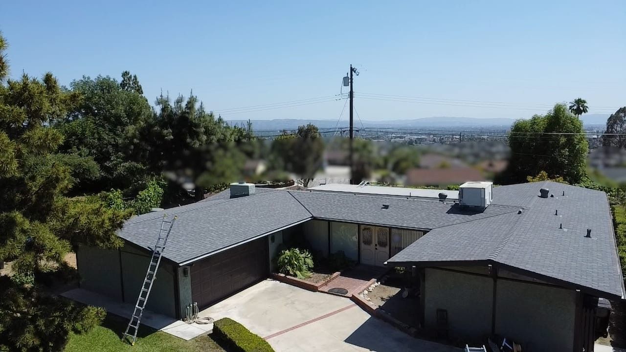 Aerial view of a U-shaped house with a gray roof, green siding, and a driveway on a sunny day.