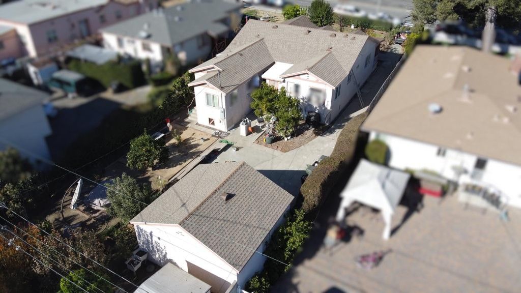 Aerial view of a white house with a brown roof and a detached garage; front yard, suburban setting.