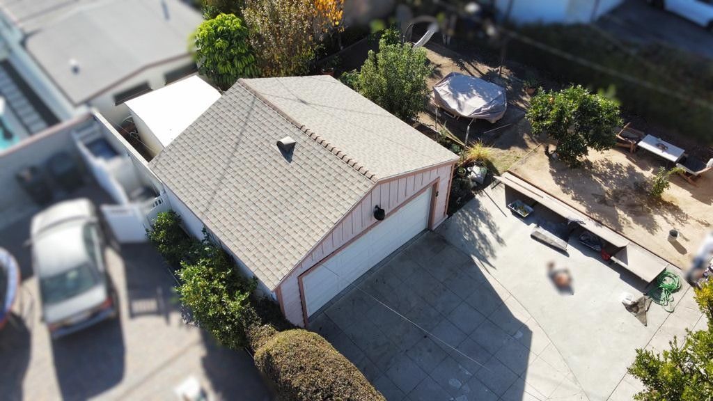 Garage with a concrete driveway, next to a house with a swimming pool and yard, seen from above.
