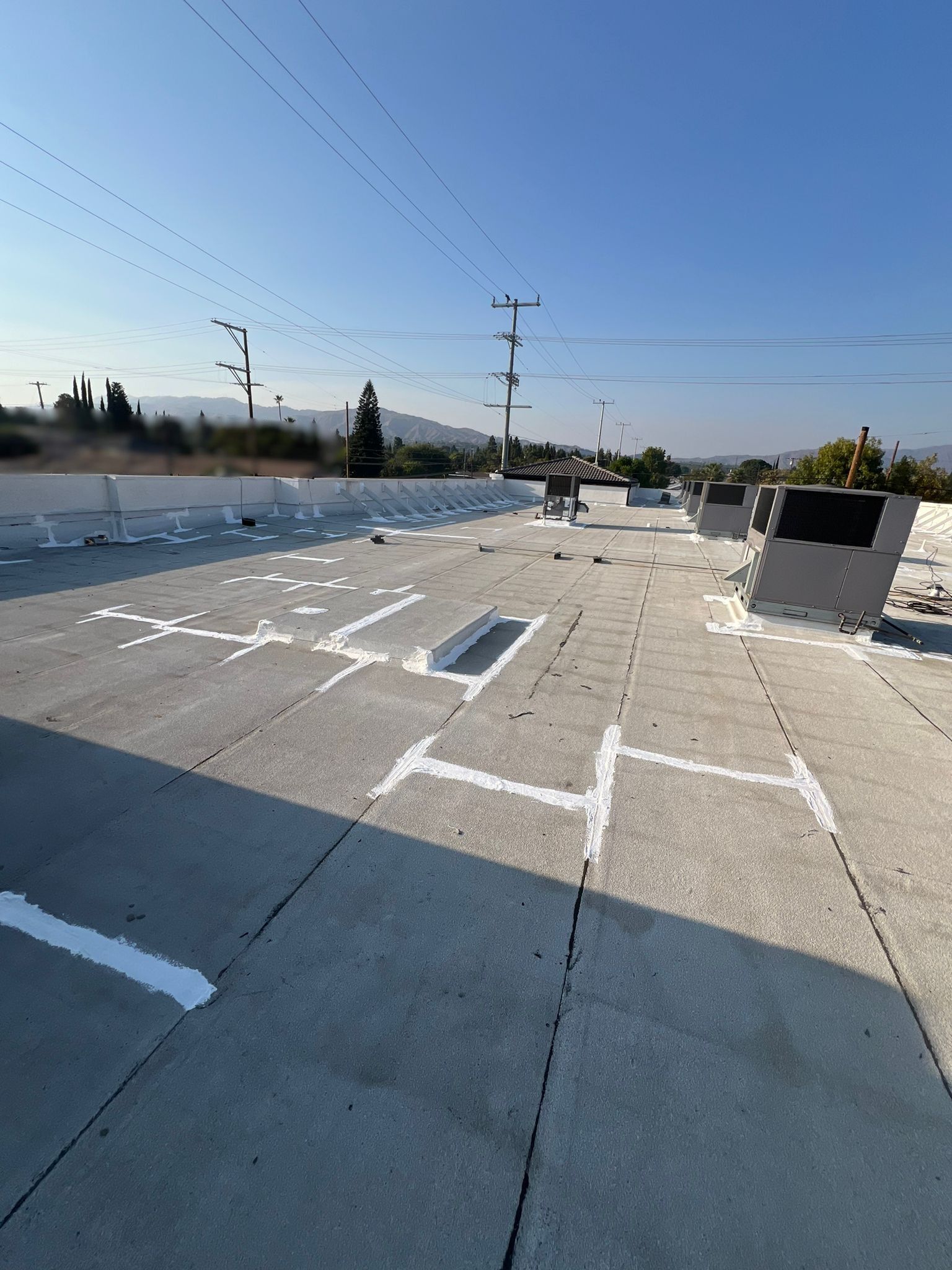 View of a flat, weathered rooftop with utility poles in the background, under a clear blue sky.