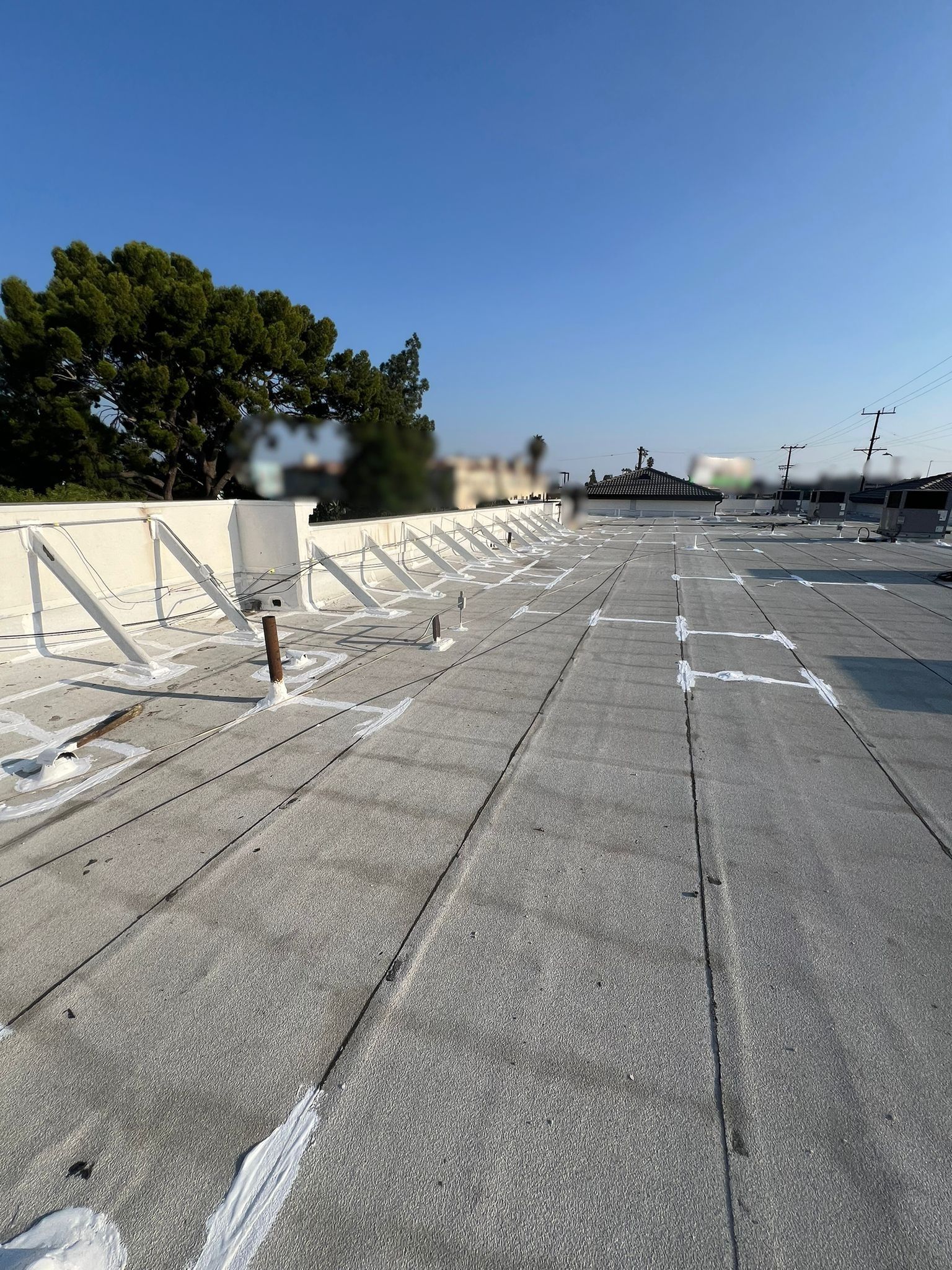 Flat, gray rooftop with white supports and patches under a clear blue sky.