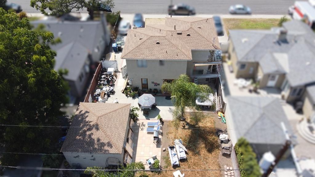 Overhead view of beige buildings with a backyard filled with items and some parked cars on the street.