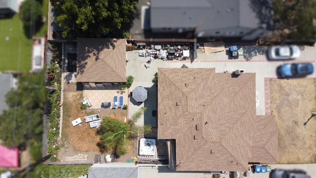 Aerial view of a house with a brown roof, backyard, and driveway. Cars are parked in the driveway.