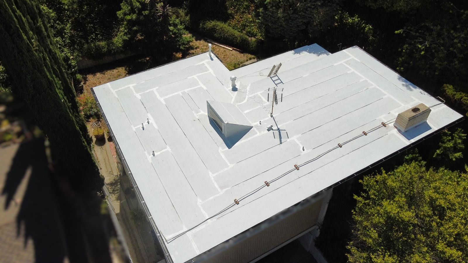 Aerial view of a white flat roof on a house with a chimney and some mechanical equipment.