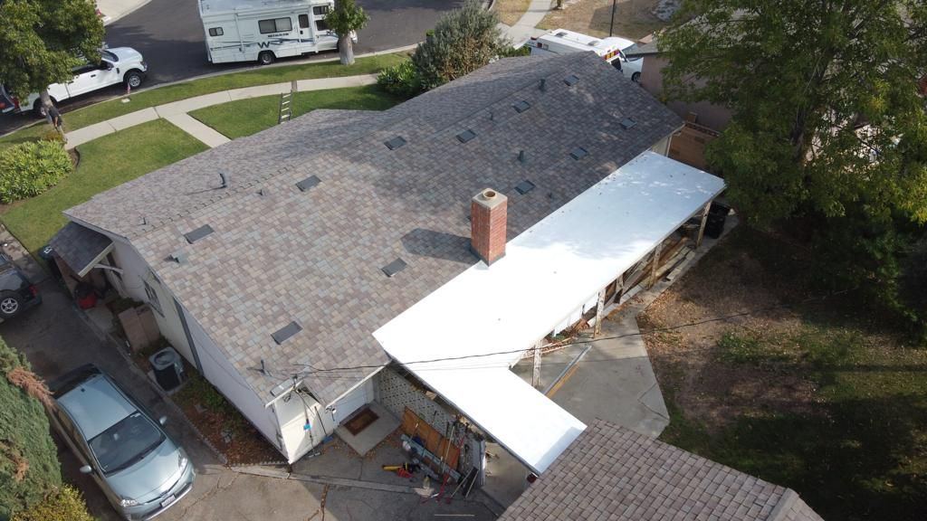 Aerial view of a house with a gray roof and white carport, a car, and a camper in the background.