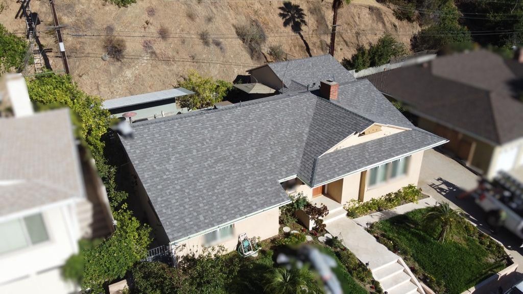 A house with a gray roof and beige walls sits on a hillside. A path leads to the front door.