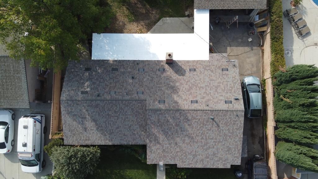 Overhead view of a house with a grey shingled roof, cars, and a swimming pool.