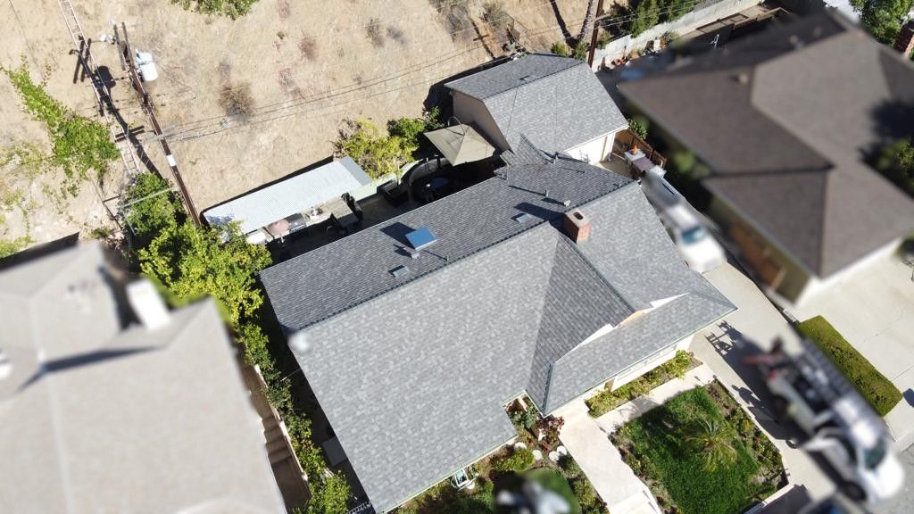 Aerial view of a house with a gray roof, surrounded by green lawn and neighboring houses.