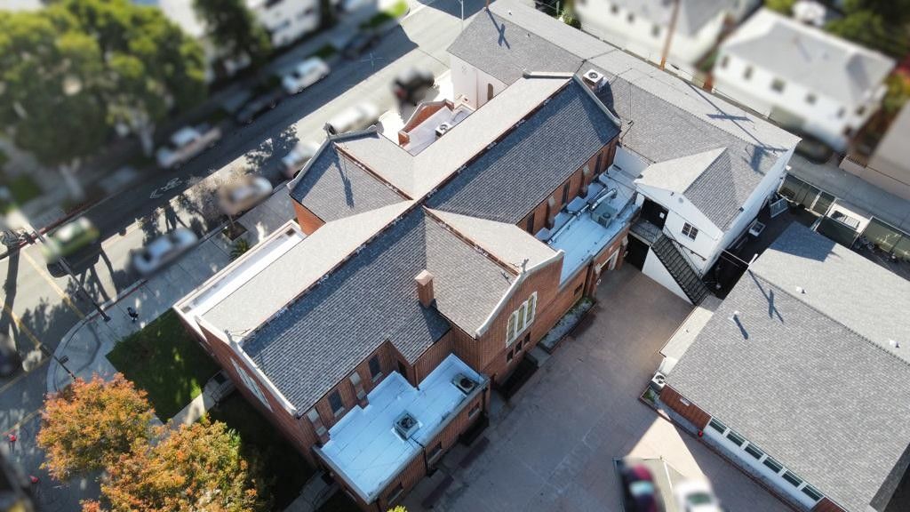 Aerial view of a brick building with a complex roof structure and a parking area.
