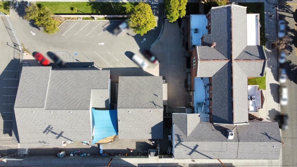 Aerial view of buildings with gray rooftops and a parking lot with a few cars.