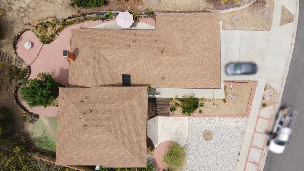 Overhead view of a house with brown roof, driveway with car, patio with umbrella and landscaping.