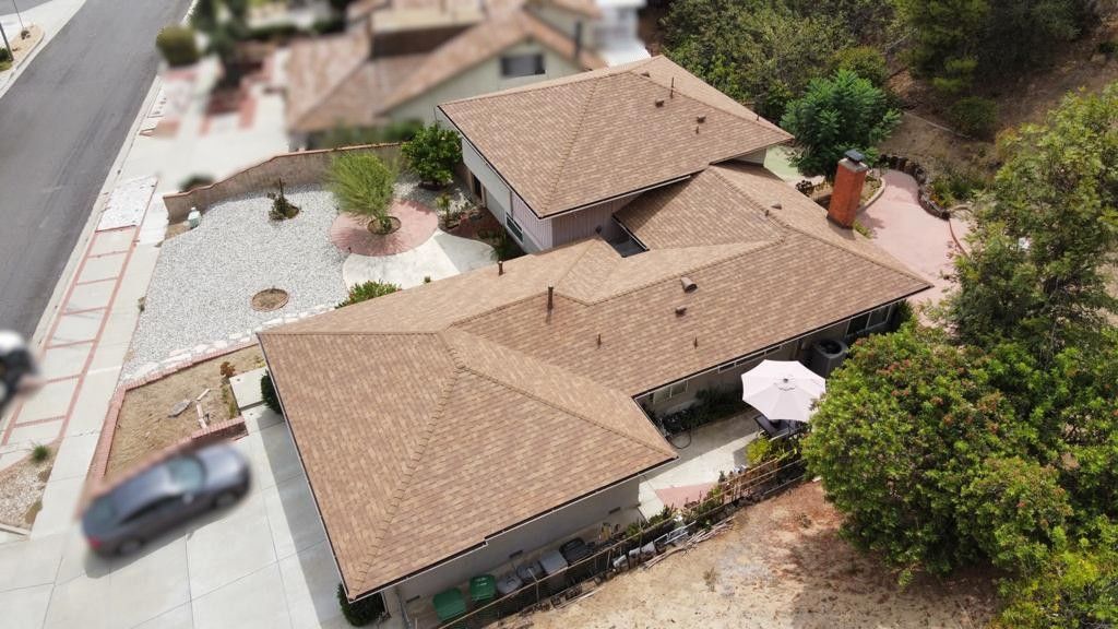 Aerial view of a house with a brown roof, surrounded by trees and a driveway with a parked car.
