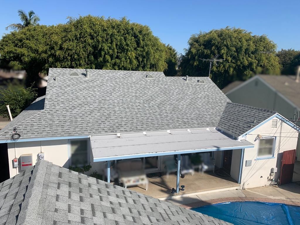 Gray shingled roofs of a house with a covered patio and swimming pool, trees in the background.