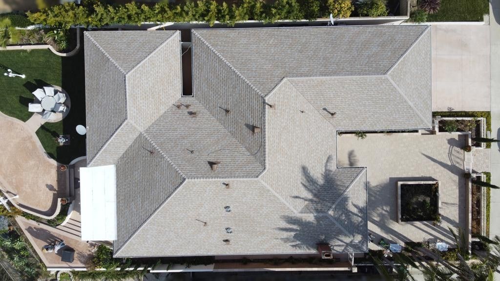 Overhead view of a light gray tile roof on a large house with a manicured lawn, patio, and driveway.