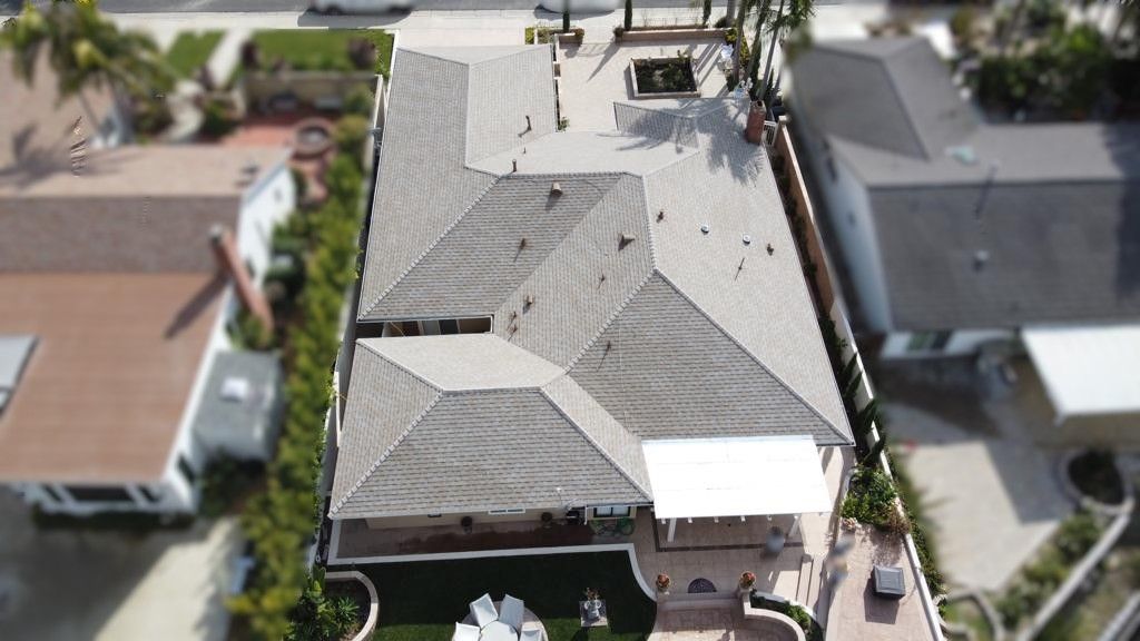 Overhead view of a house with a gray shingled roof, green yard, and neighboring houses.