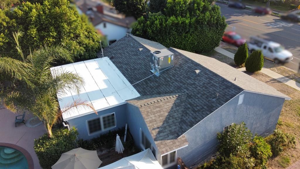 Overhead view of a blue house with a grey roof, trees, and a street with cars.