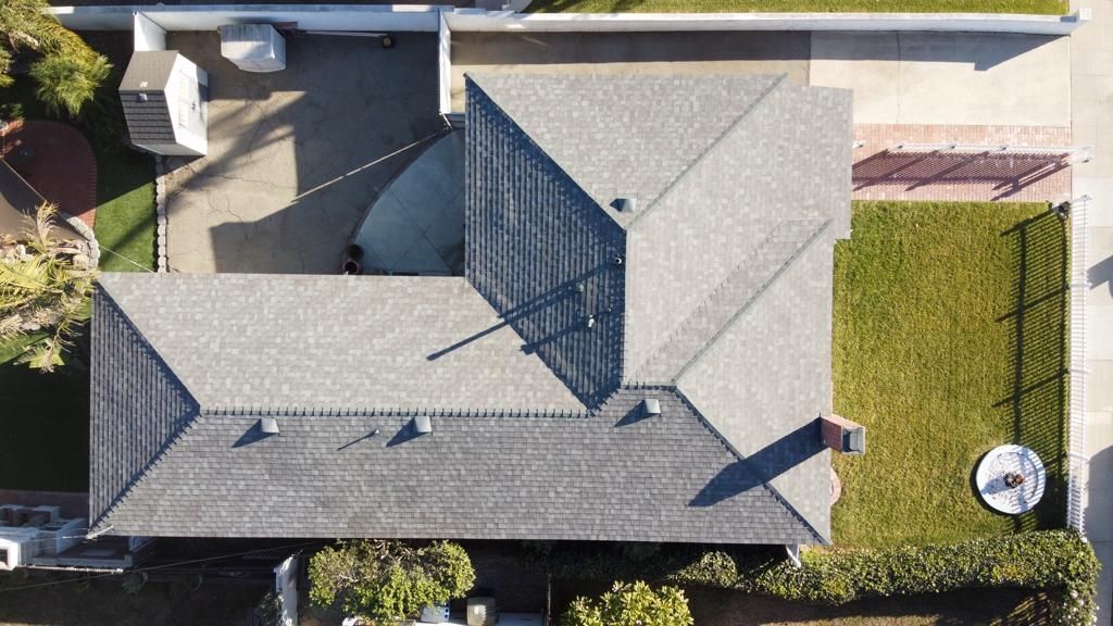 Overhead view of a gray-roofed house with green grass and a driveway; trees surround the property.