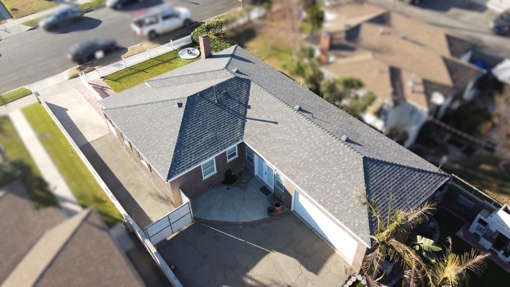 Aerial view of a house with gray roof, brick exterior, driveway, and small yard.