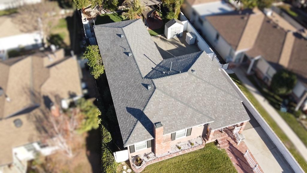 Aerial view of a house with a gray roof, green lawn, and neighboring homes.