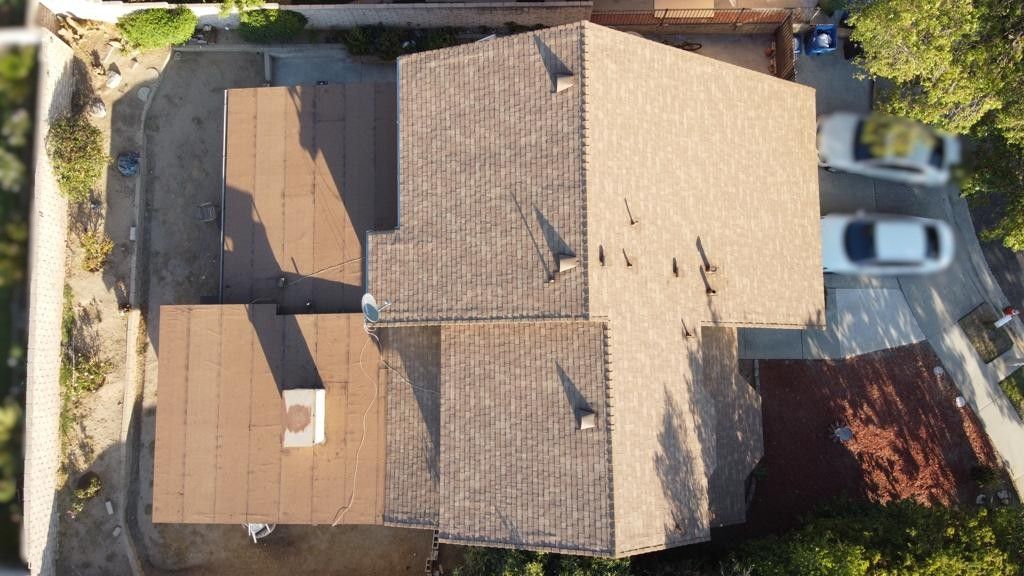 Overhead view of a brown roofed house with three sections. Cars are parked on the right side.