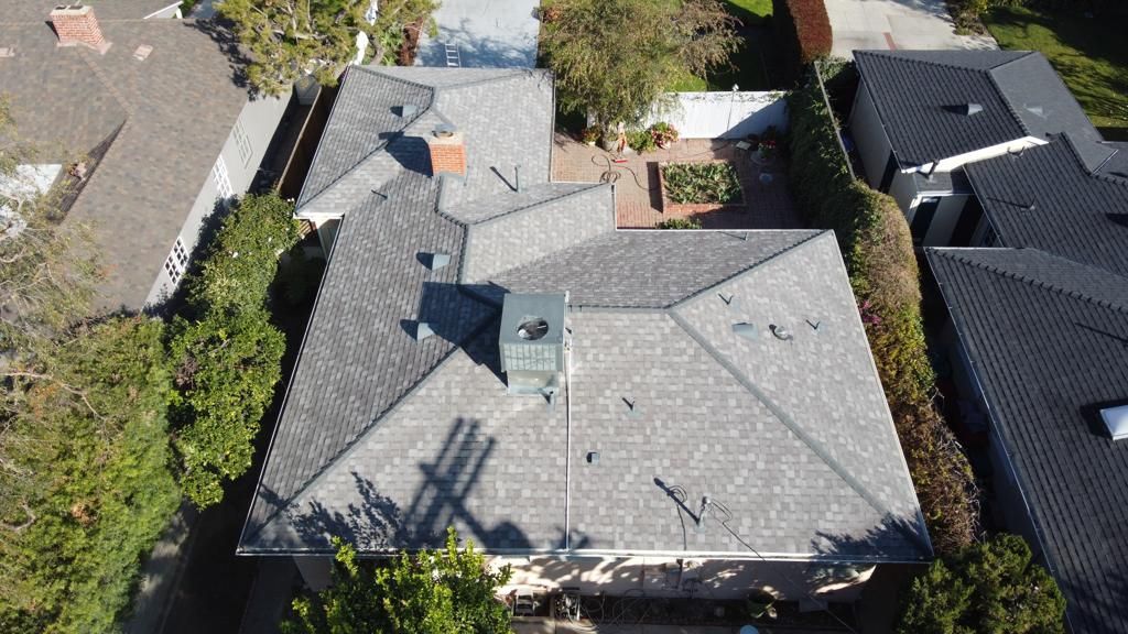 Overhead view of multiple houses with gray roofs, surrounded by green trees and a sunny sky.