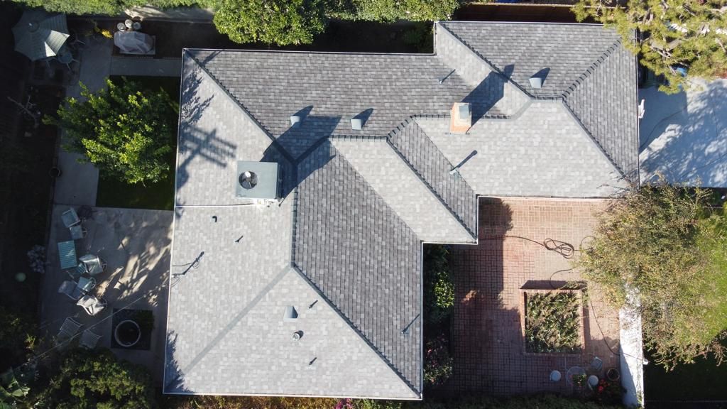 Overhead view of a house with a grey roof, surrounded by trees and a brick patio.