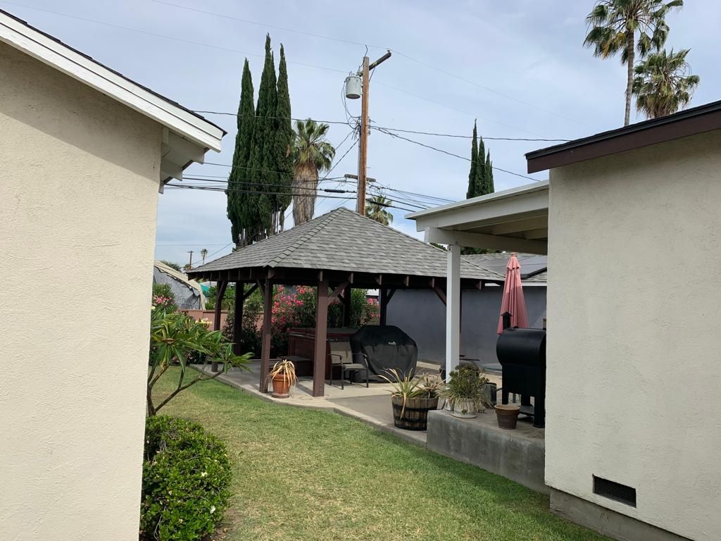 Backyard with gazebo, lawn, two houses, and trees on a cloudy day.