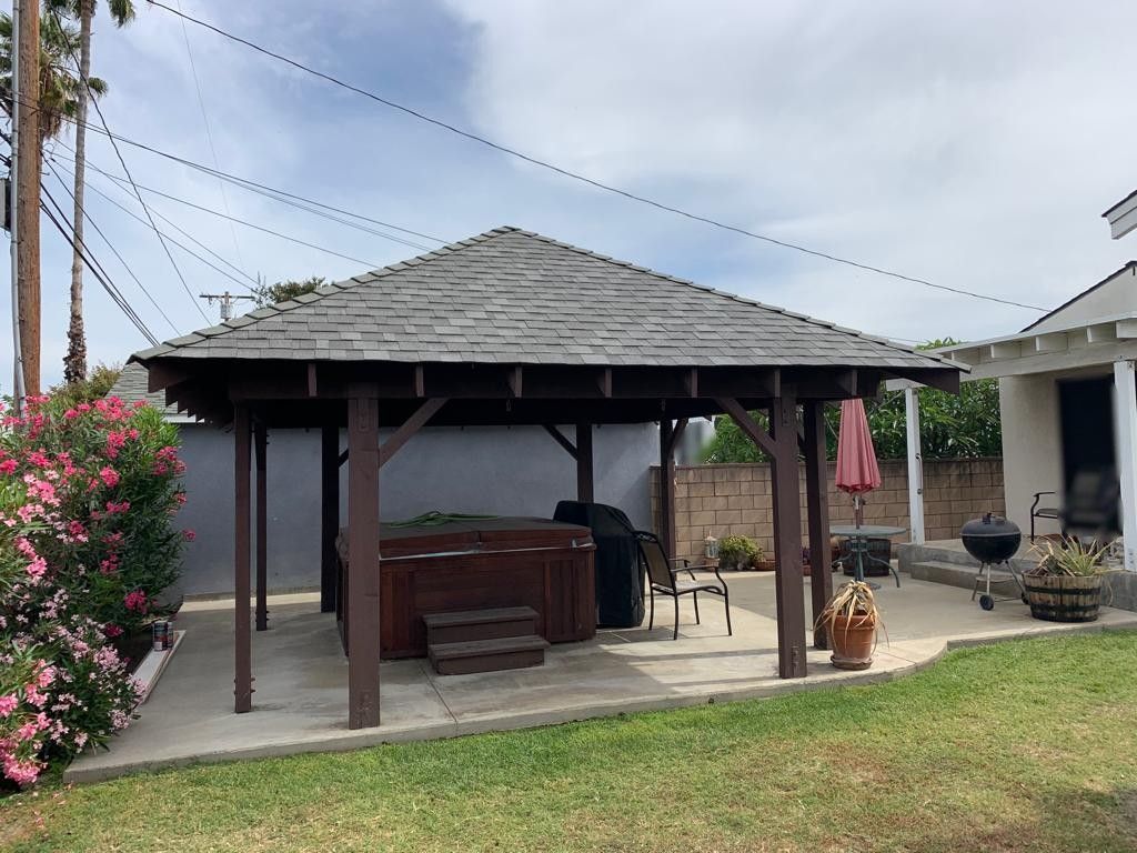 A wooden gazebo with a hot tub, patio, and grass.