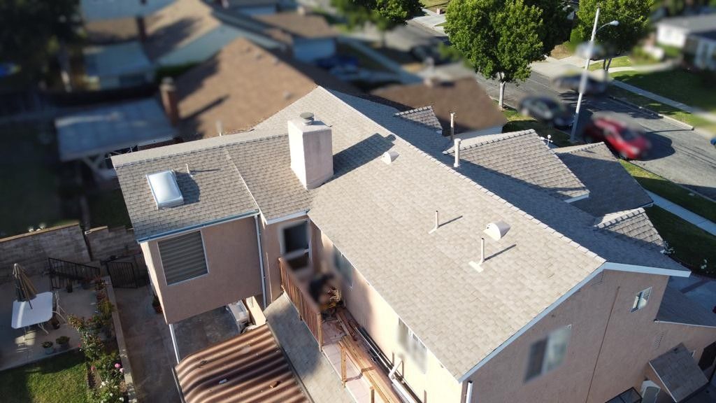 Aerial view of a beige two-story house with brown roof, chimney, and a red car in the background.