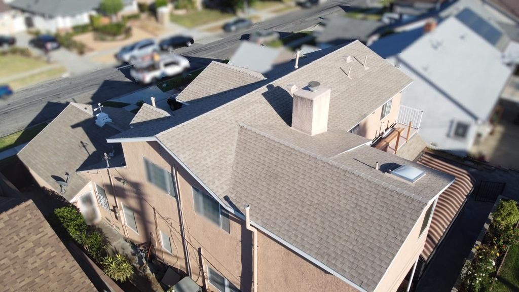 View of a two-story house with brown shingles, chimney, and adjacent street with parked cars.