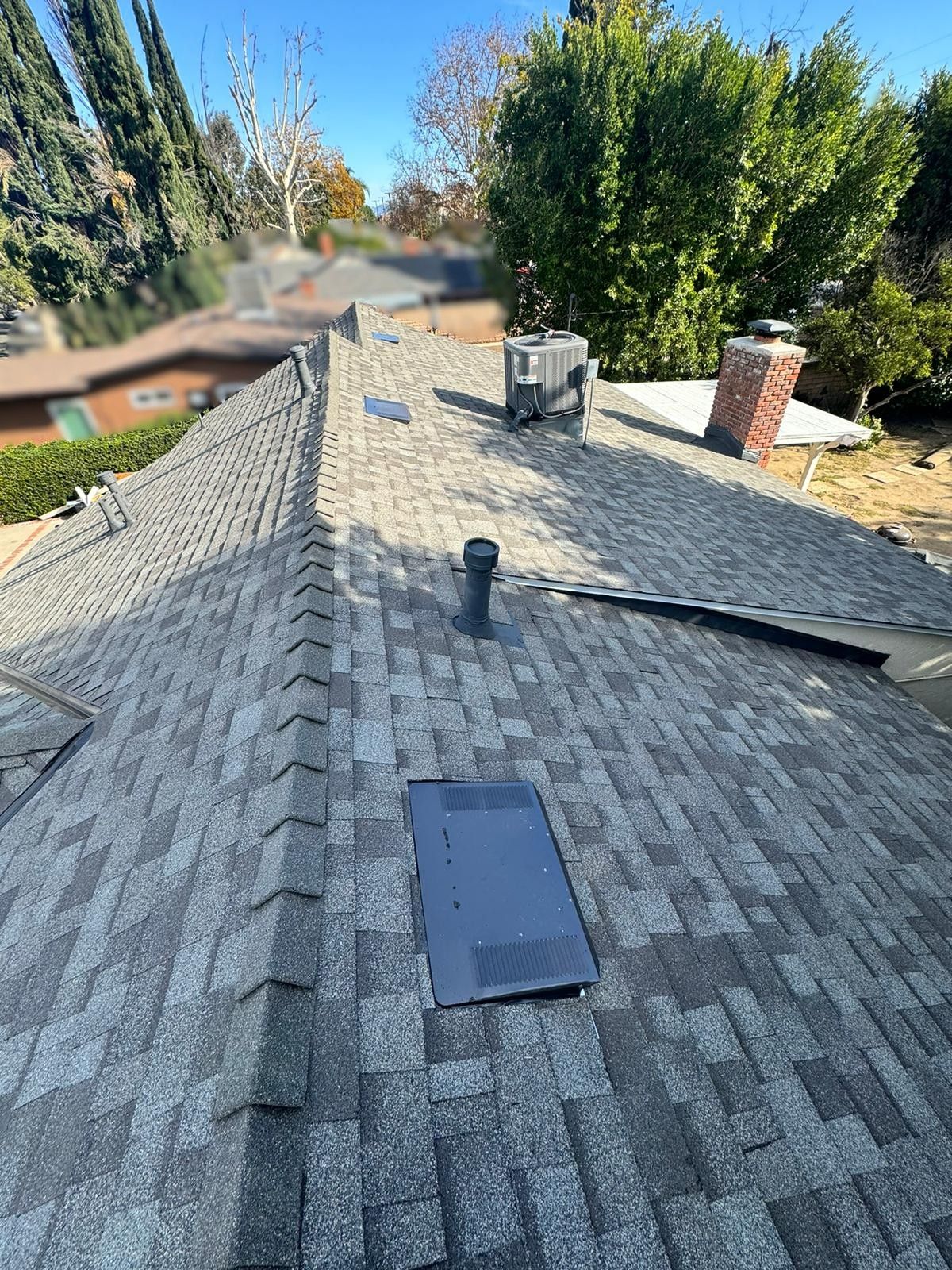View of a gray asphalt shingle roof with a vent, air conditioner, and chimney.