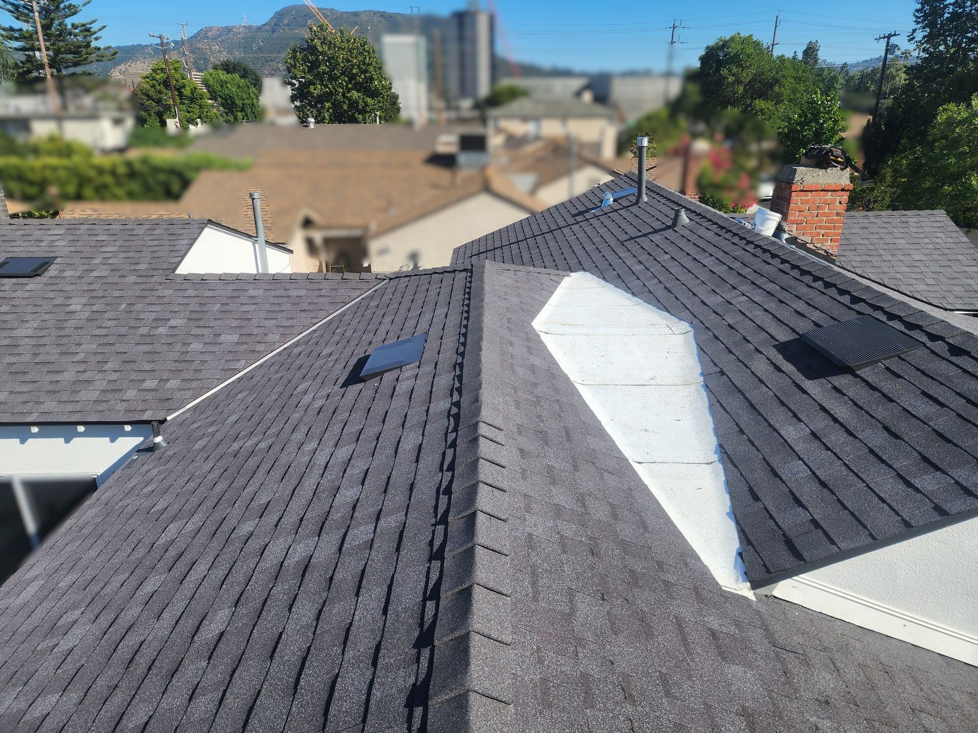 View of a dark grey shingled roof with white patching, set in a residential neighborhood.