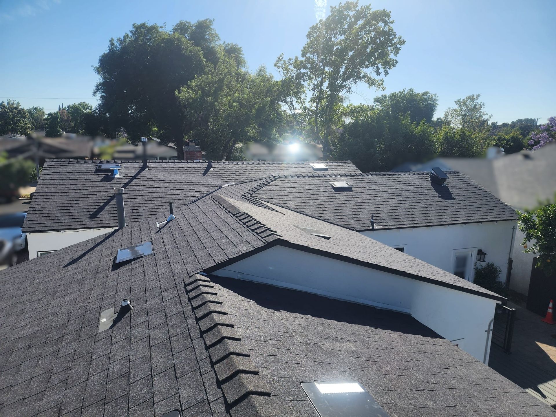 Dark asphalt shingle roof with vents and chimneys on a sunny day.