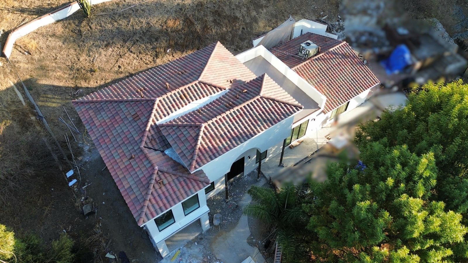 Aerial view of a white house with a red tile roof surrounded by trees and dry brush.