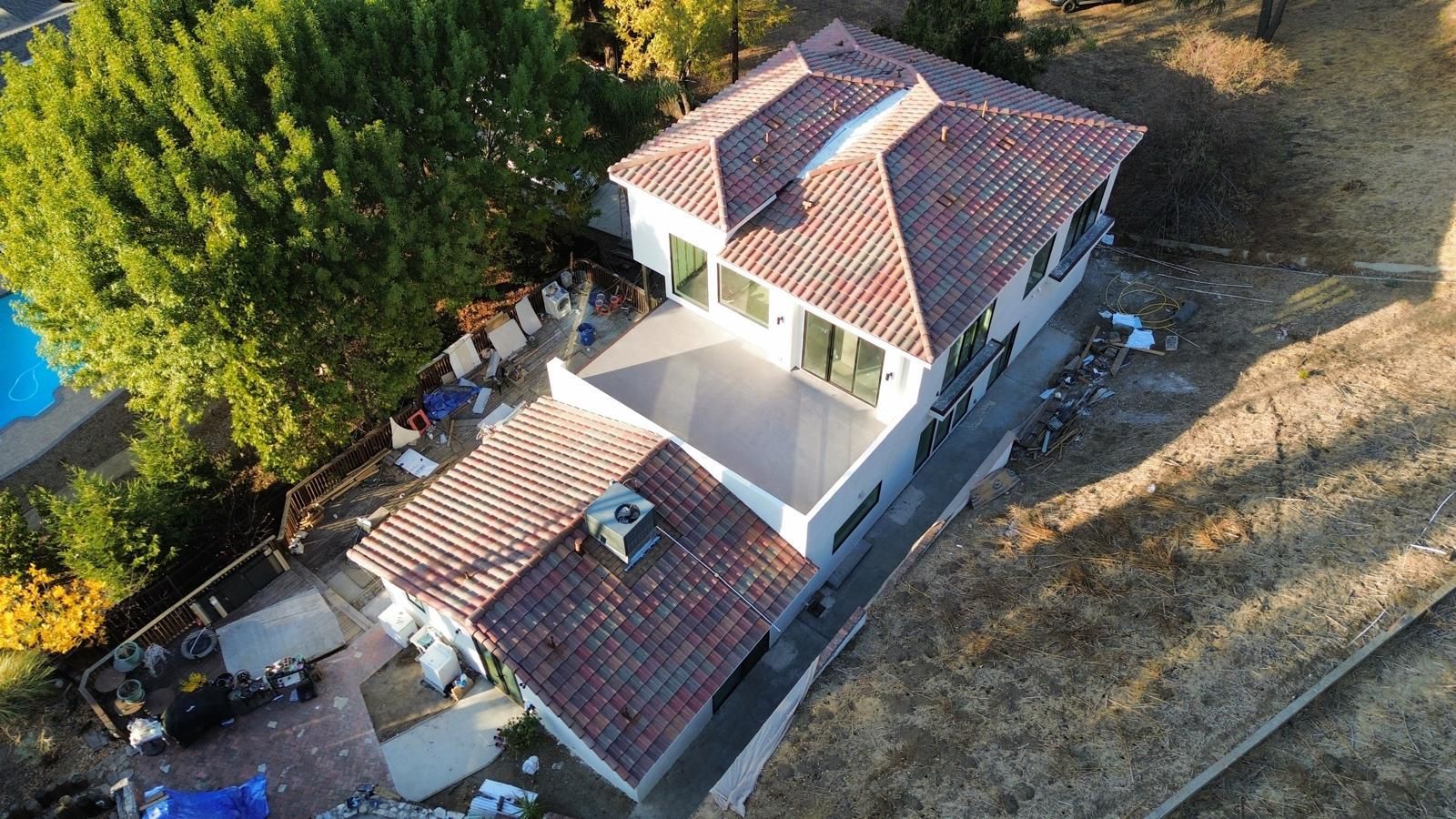 High-angle view of a two-story house with a red-tiled roof, a pool, and a deck.