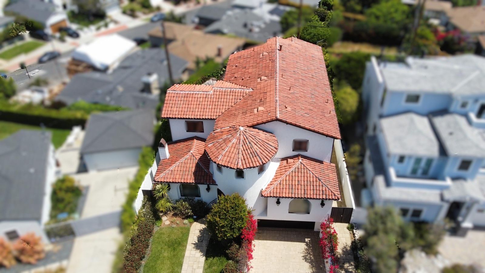 Spanish-style home with red tile roof, white walls, and lush landscaping.
