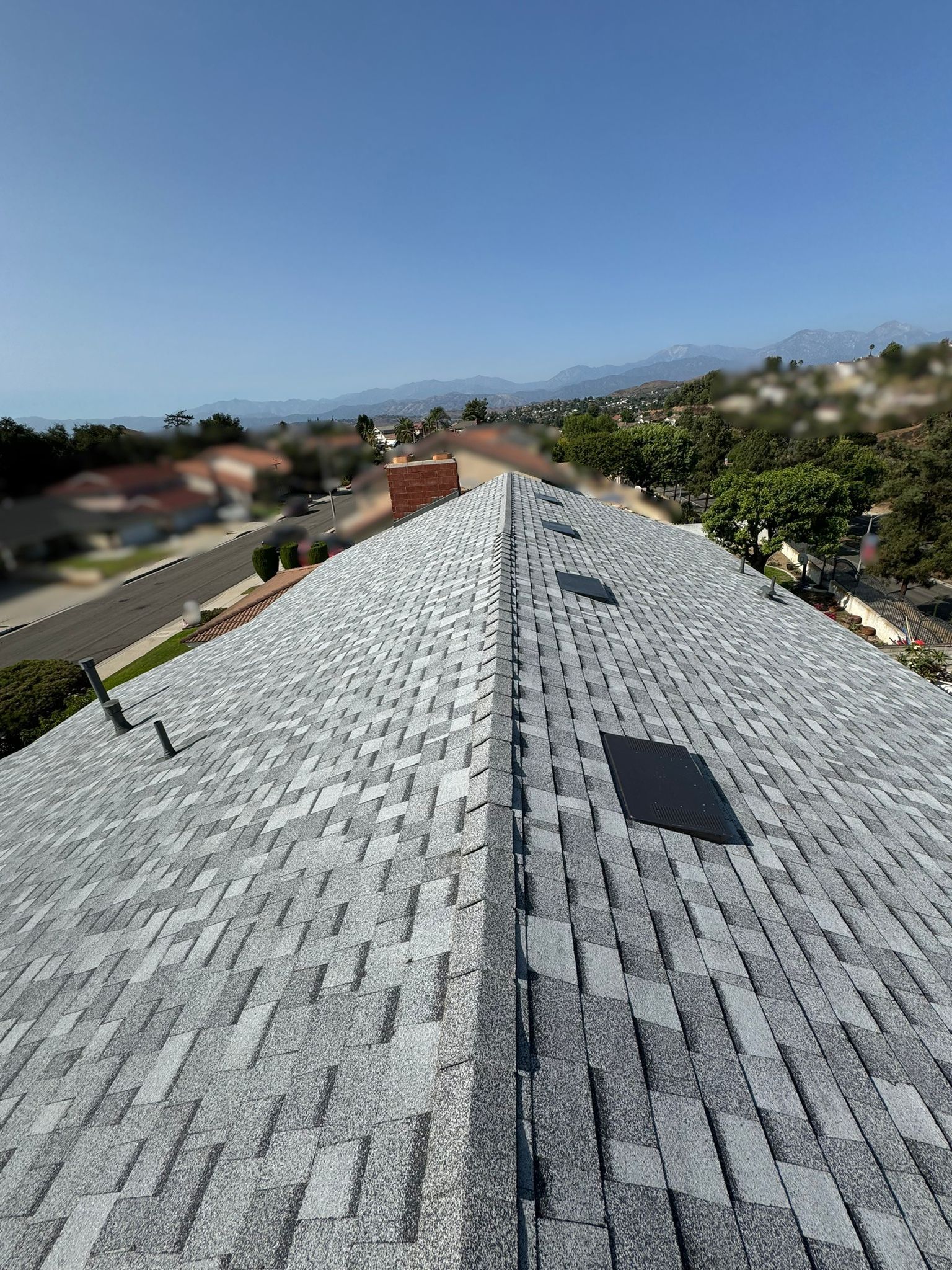 Gray shingled rooftop, view down the ridge, sunny day, houses and distant mountains.