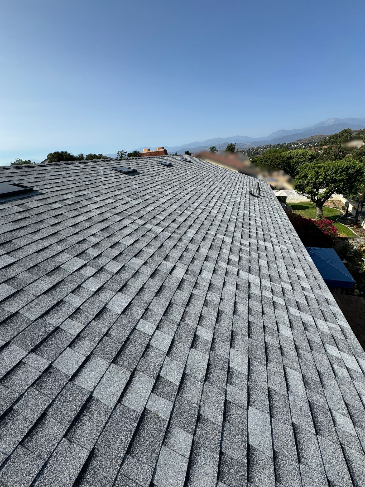 View from a roof with gray shingles, sunny sky, and a view of the mountains.