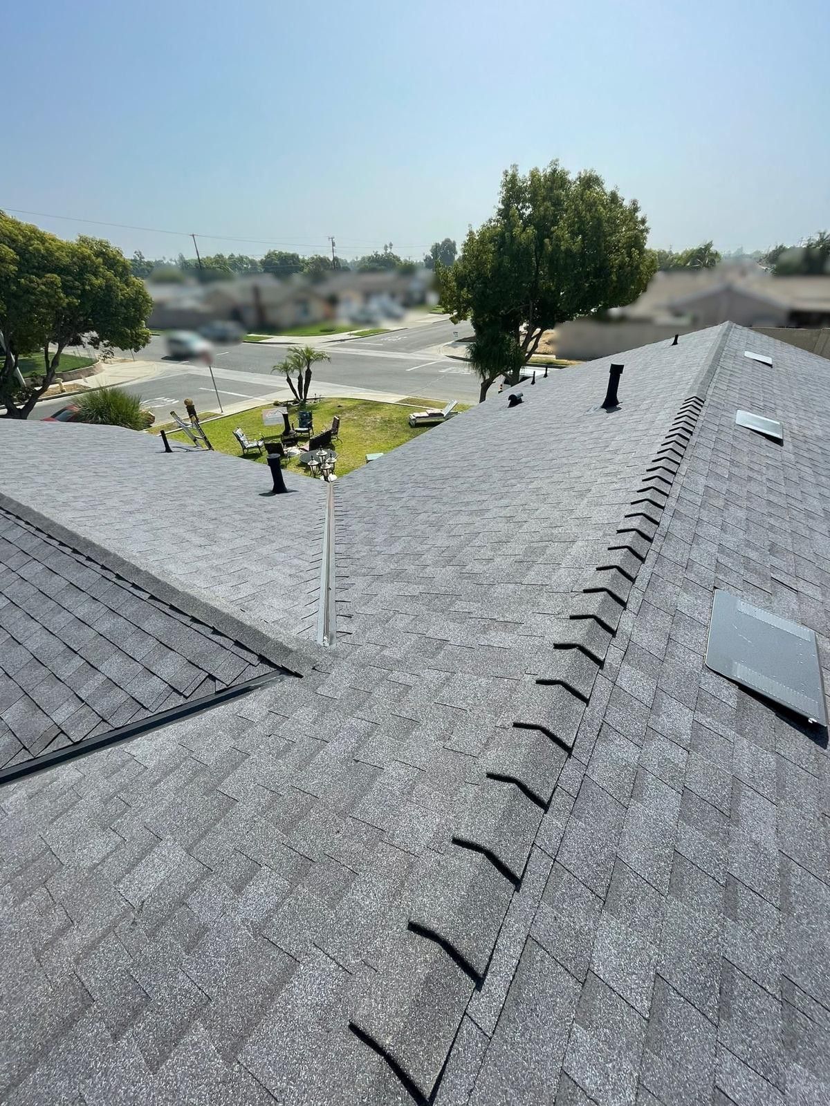 Gray asphalt shingle roof with multiple vents, trees, and a clear sky in the background.