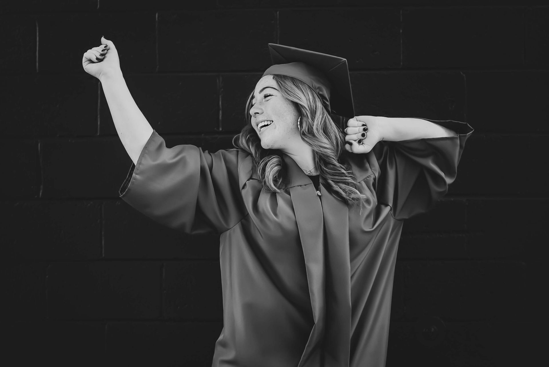 Person in graduation cap and gown celebrates with an arm raised.